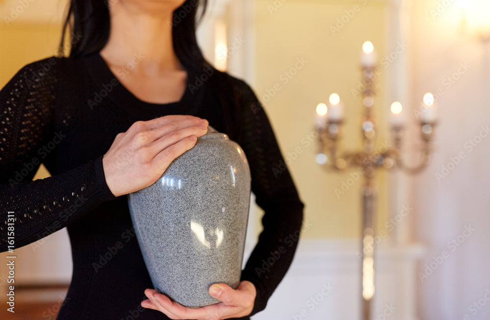 Woman in black dress holding a grey metal cremation urn at memorial service