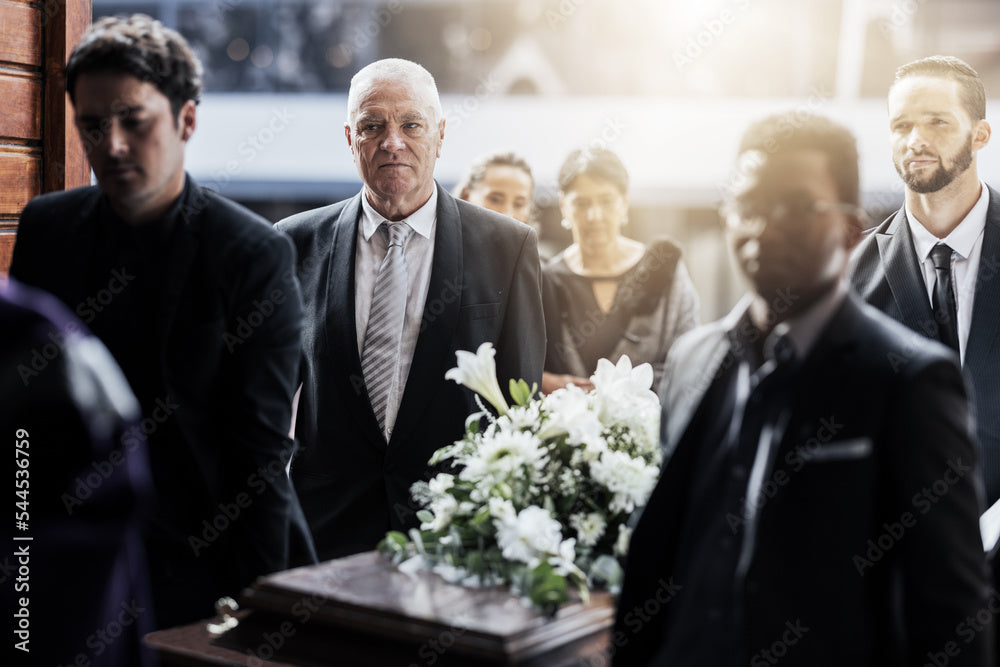 Funeral procession with people in suits carrying casket adorned with white flowers