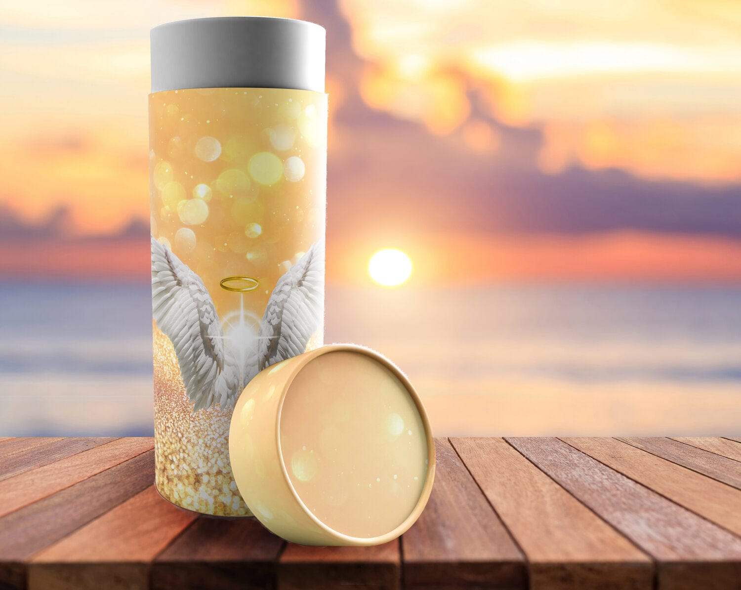 Biodegradable cremation urn tube with angel wings design on wood table at sunset by the sea